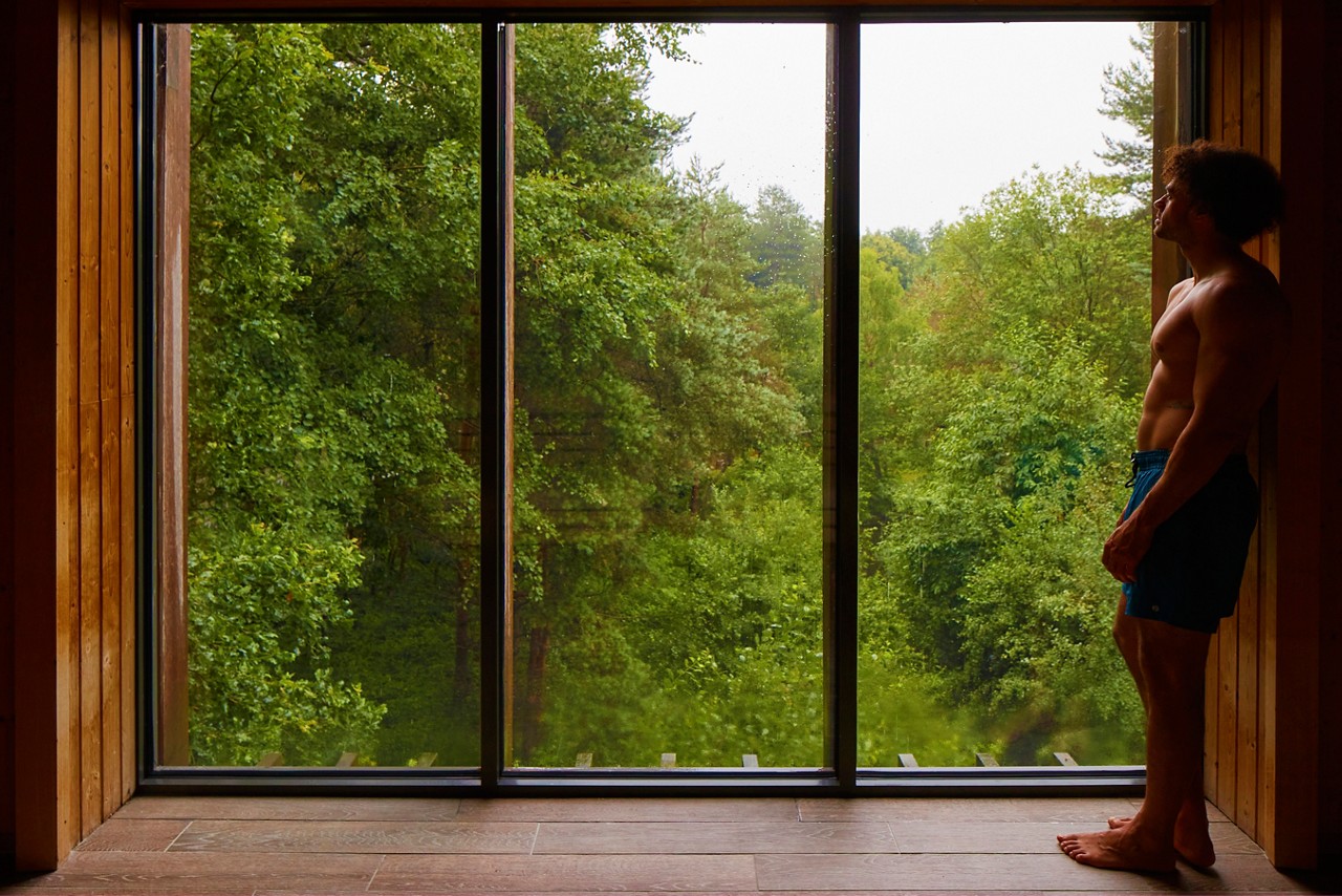 Man stood admiring the views of the forest from inside the Treetop Sauna.